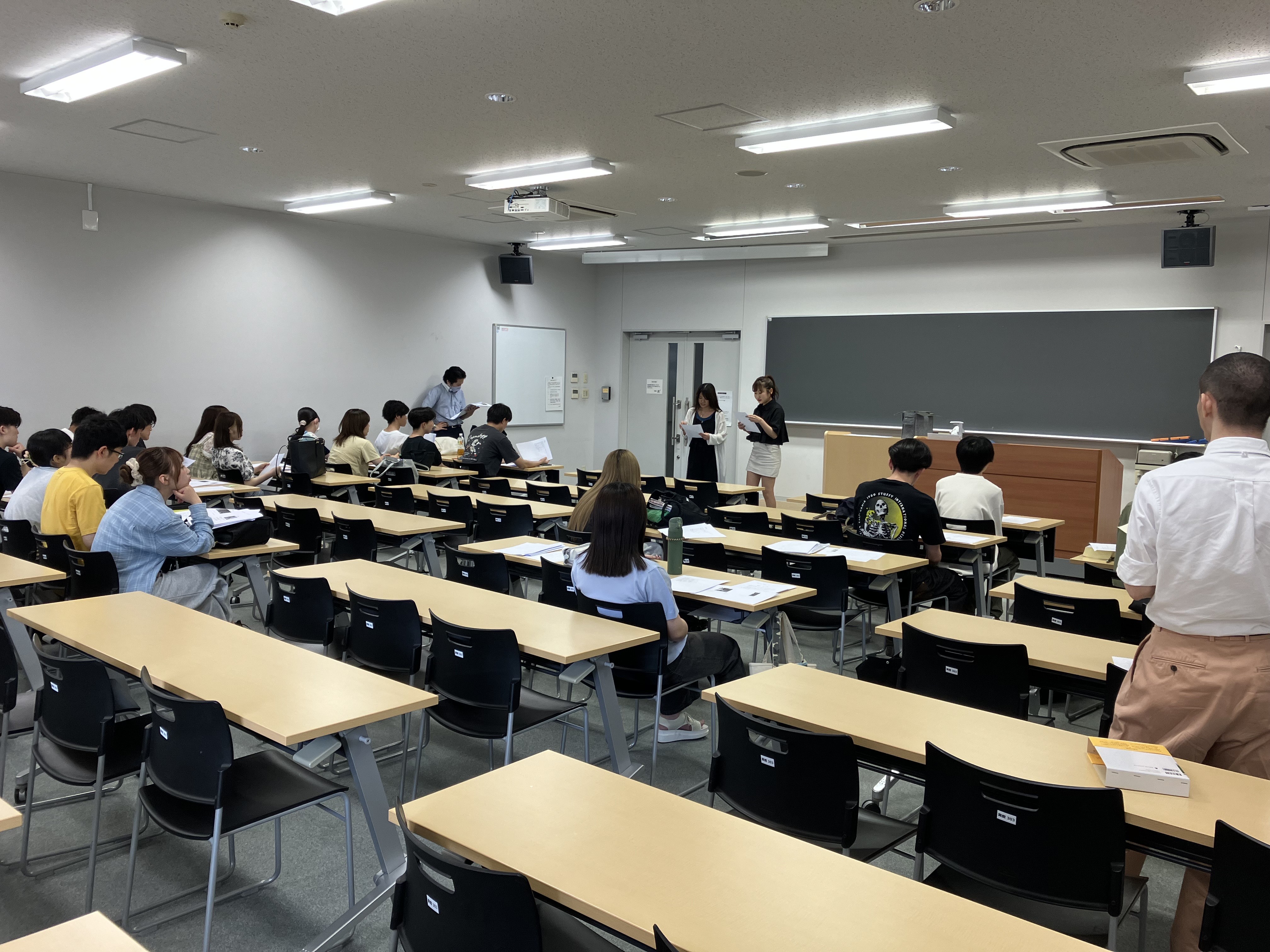 学生たちの発表を、その他の学生や先生たちが教室で聞いている様子