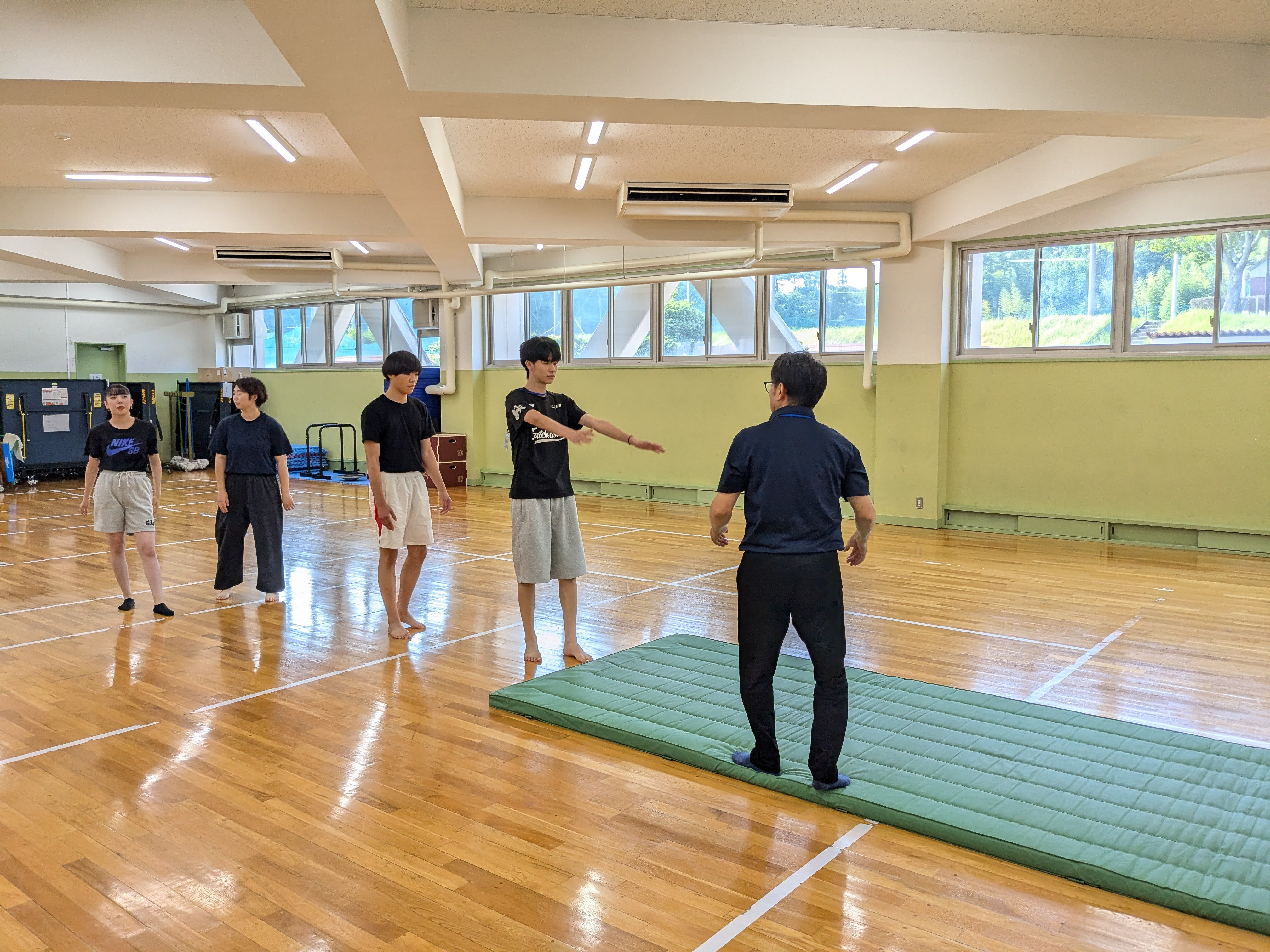 体育館で、学生たちがマットで実技(器械体操)に取り組んでいる